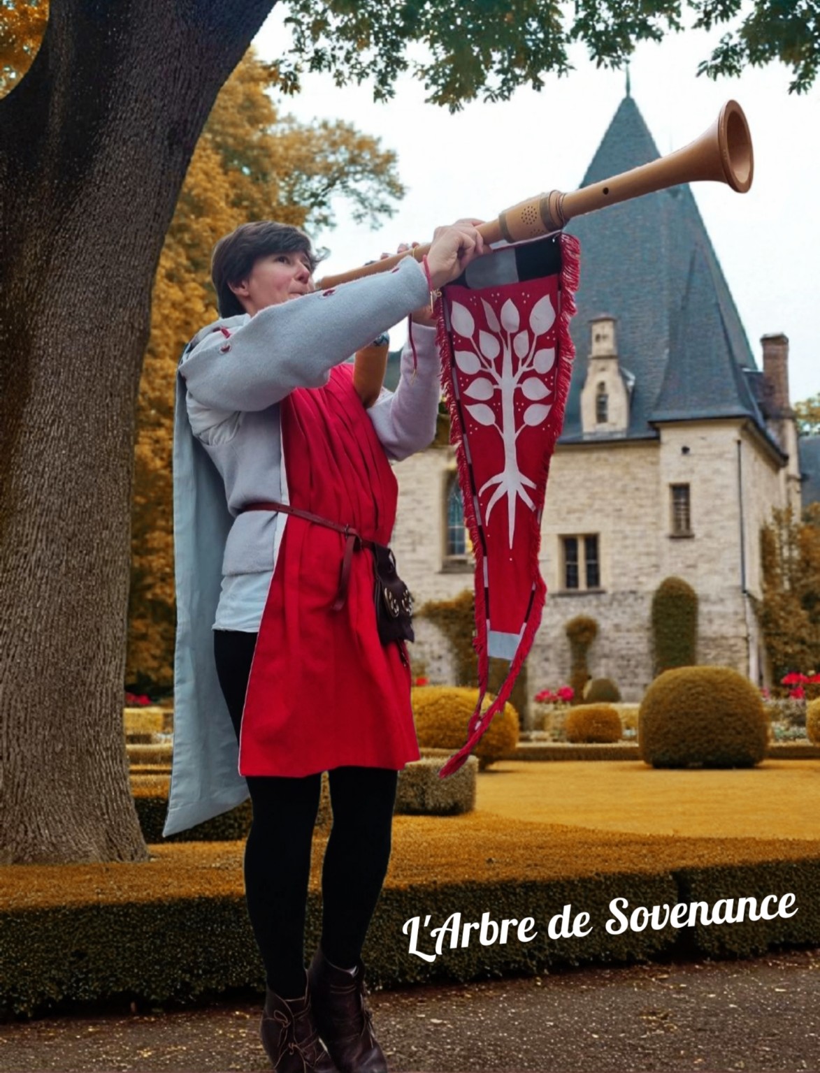 Une musicienne en costume joue d’un instrument à vent orné de la bannière de L’Arbre de Sovenance devant un château.
