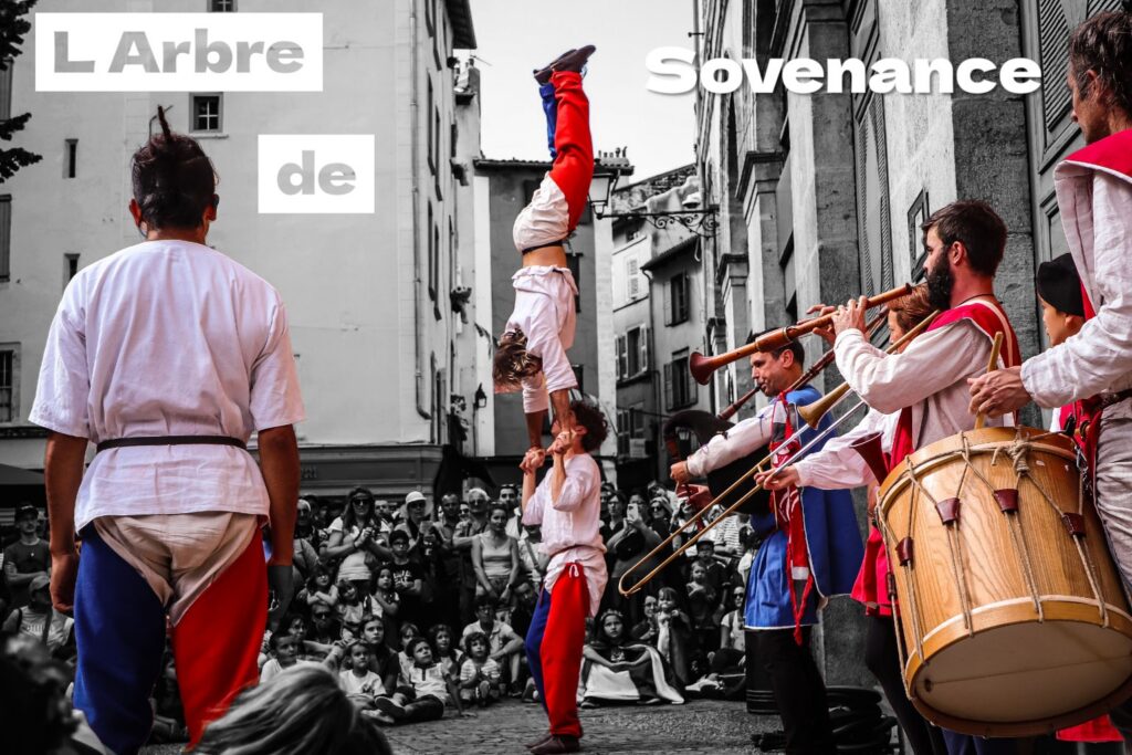 Un porté acrobatique accompagné par les musiciens de L’Arbre de Sovenance devant le public réuni dans une rue.
